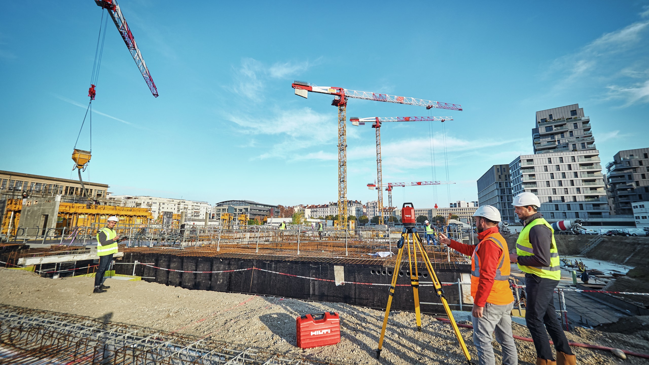 Two men stood infront of a tripod on a construction site with cranes in the background