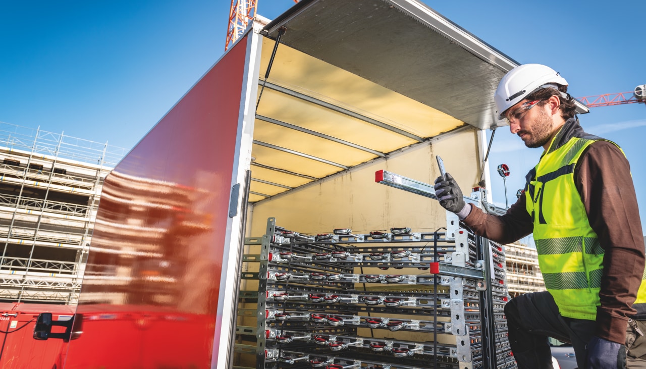 A man looking at a smartphone behind a lorry containing building components