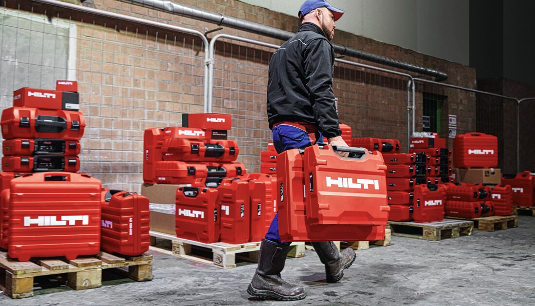 a man carrying red hilti tool cases with red hilti tools on pallets in the background