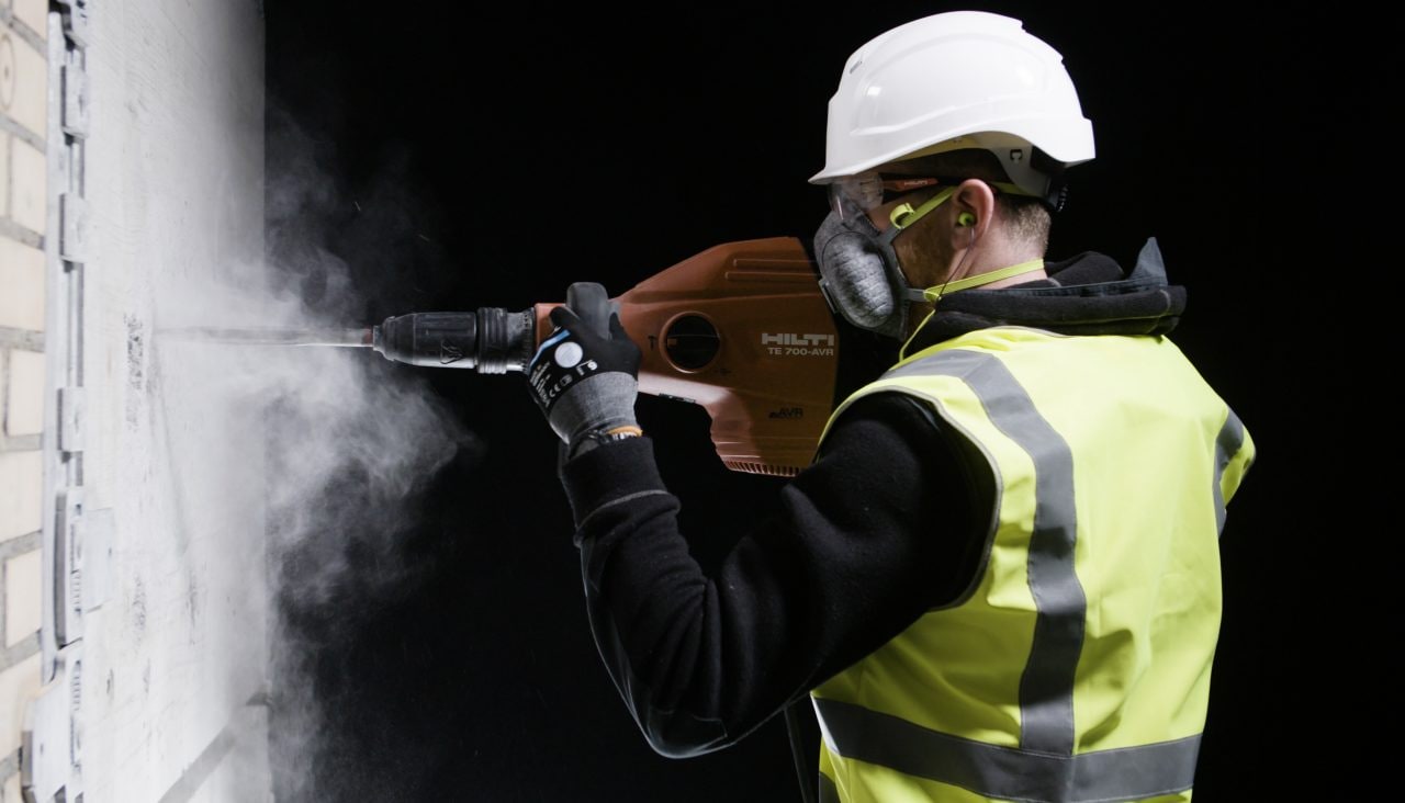 person wearing a mask drilling into a wall with dust expelling