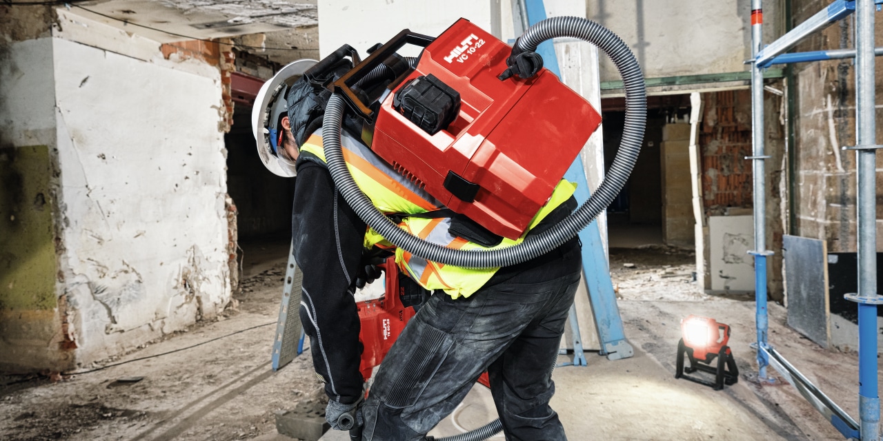 person drilling into a concrete floor wearing a backpack hilti vacuum cleaner