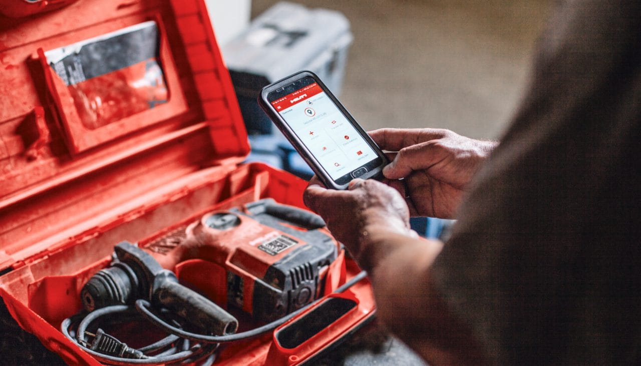 perosn using mobile phone with a red hilti drill in the background