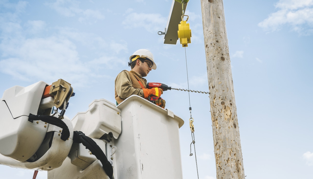 man drilling wood on an electric post