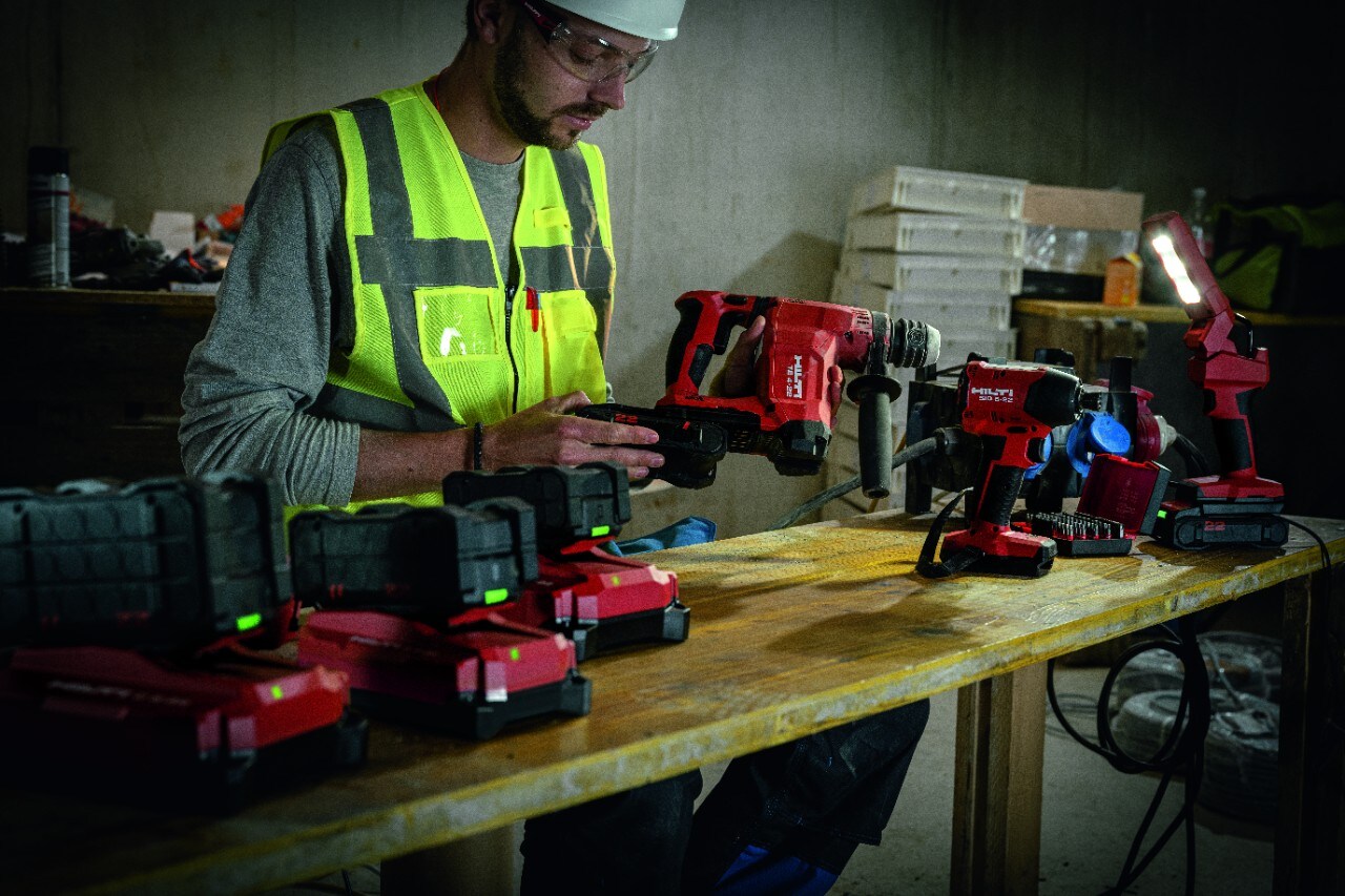 Construction worker behind a work bench with many Hilti tools and batteries on it.