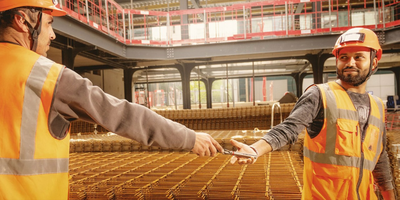 Man passing drill bit to another construction worker