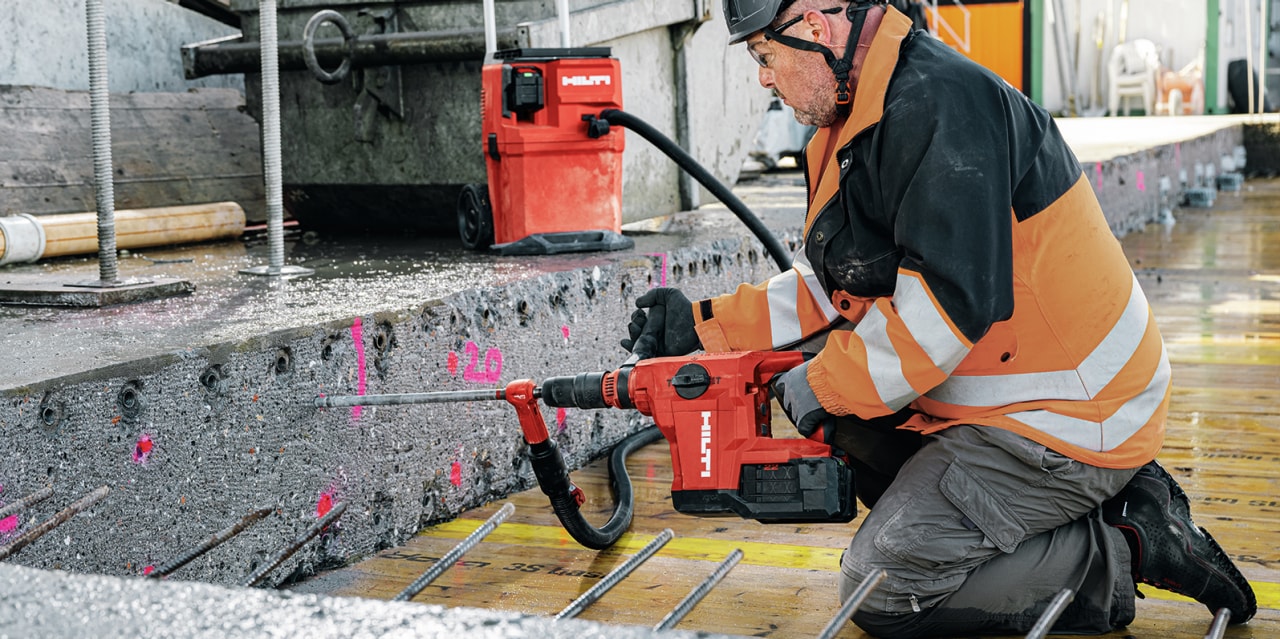 man using red Hilti drill to drill holes into concrete