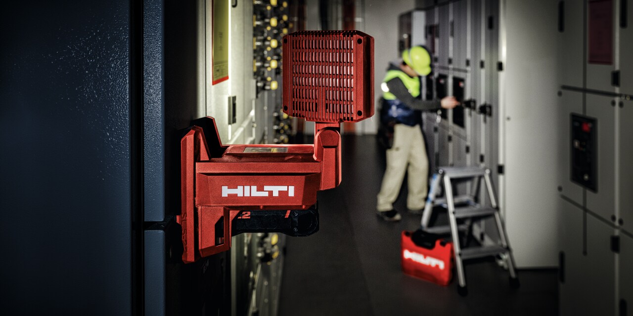 MAN WORKING IN A DARK ROOM WITH A RED HILTI LIGHT ON THE  WALL