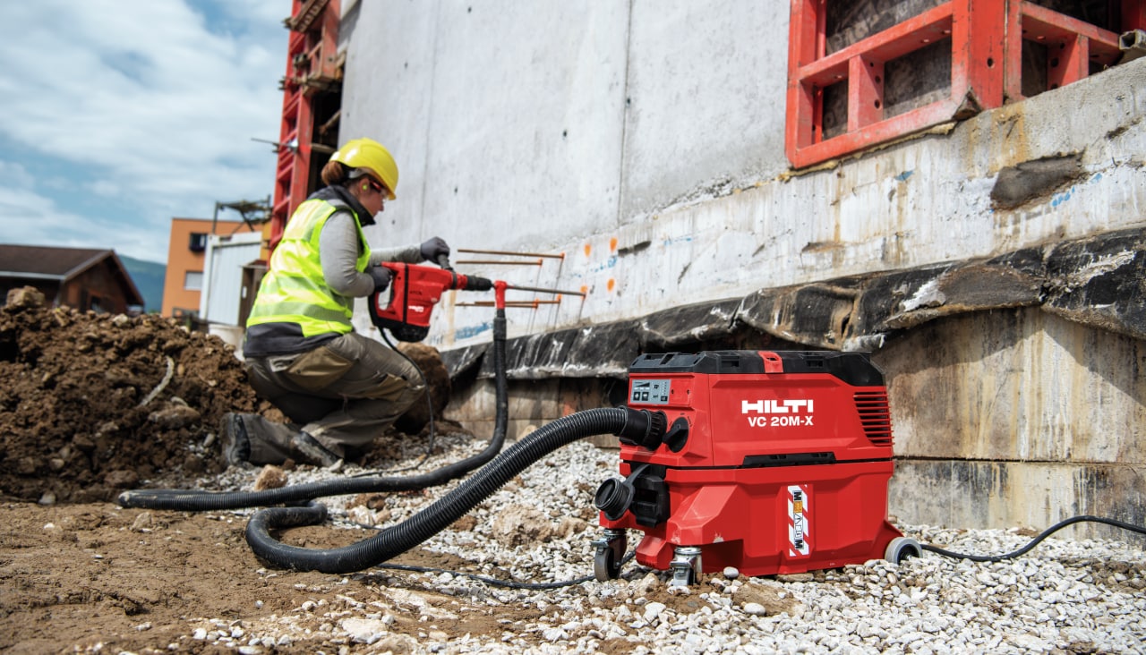 person using a Hilti drill connected to a red Hilti vacuum to drill holes into concrete