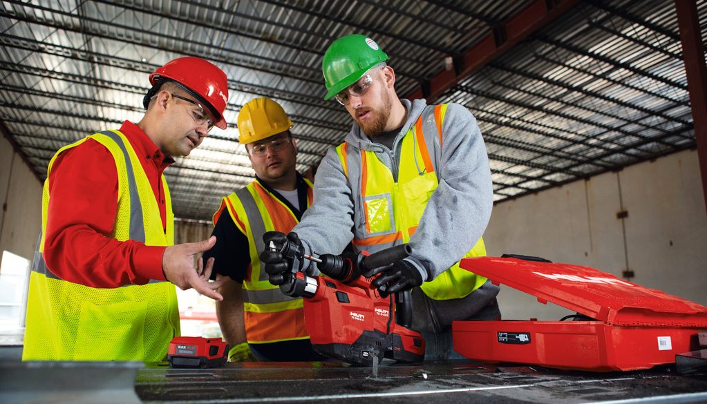 3 men in hard hats and hi vis vests stood over a red Hilti tool